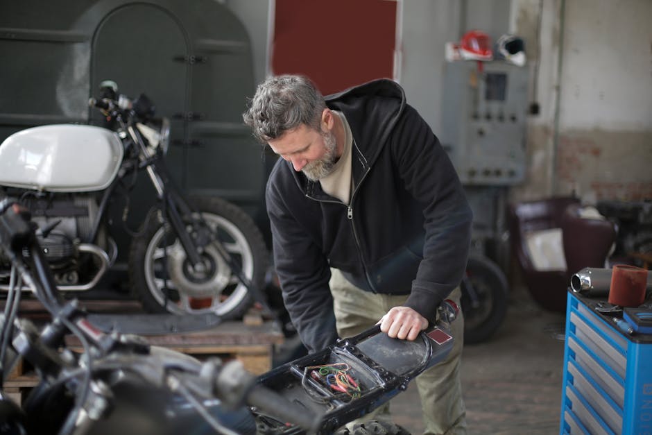 Middle aged bearded male mechanic in workwear repairing electric parts of motorbike while working in modern garage